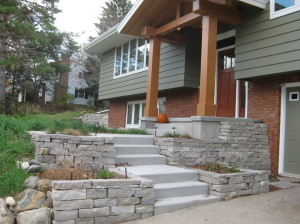 Locally sourced natural stone was used to create aesthetically appealing retaining walls and planting beds, which were filled with hardy native wildflowers and grasses for a beautiful and eco-friendly look. The new entryway allows for a more leisurely and naturalistic approach to the home. Two ornamental trees were used to visually anchor the sides of the house, while a texturally rich cobblestone dripline and small bioswale improve the flow of water on the site.